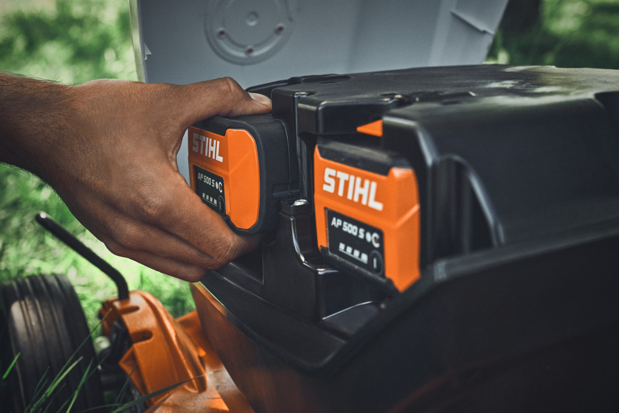 En person setter et STIHL AP 500 S-batteri i en STIHL batteridrevet gressklipper