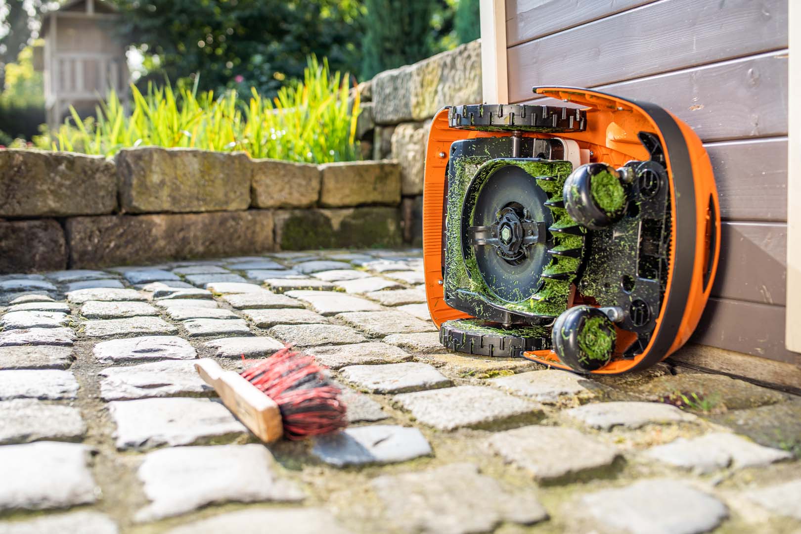 En STIHL iMOW® robotgressklipper snudd på siden klar for rengjøring, med en kost liggende i nærheten