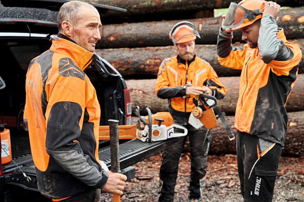 Tre menn med verneutstyr foran et kjøretøy med åpent bagasjerom hvor det ligger batteridrevne verktøy fra STIHL