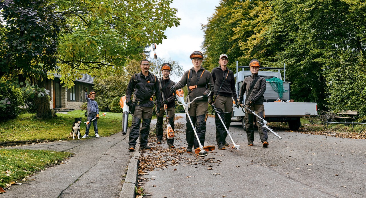 Et hage- og anleggsgartnerteam med profesjonelle batteridrevne STIHL-verktøy går gatelangs.