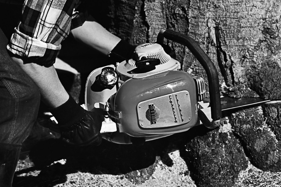 Gammelt svart-hvitt nærbilde av en person som feller et tre med en STIHL Contra motorsag