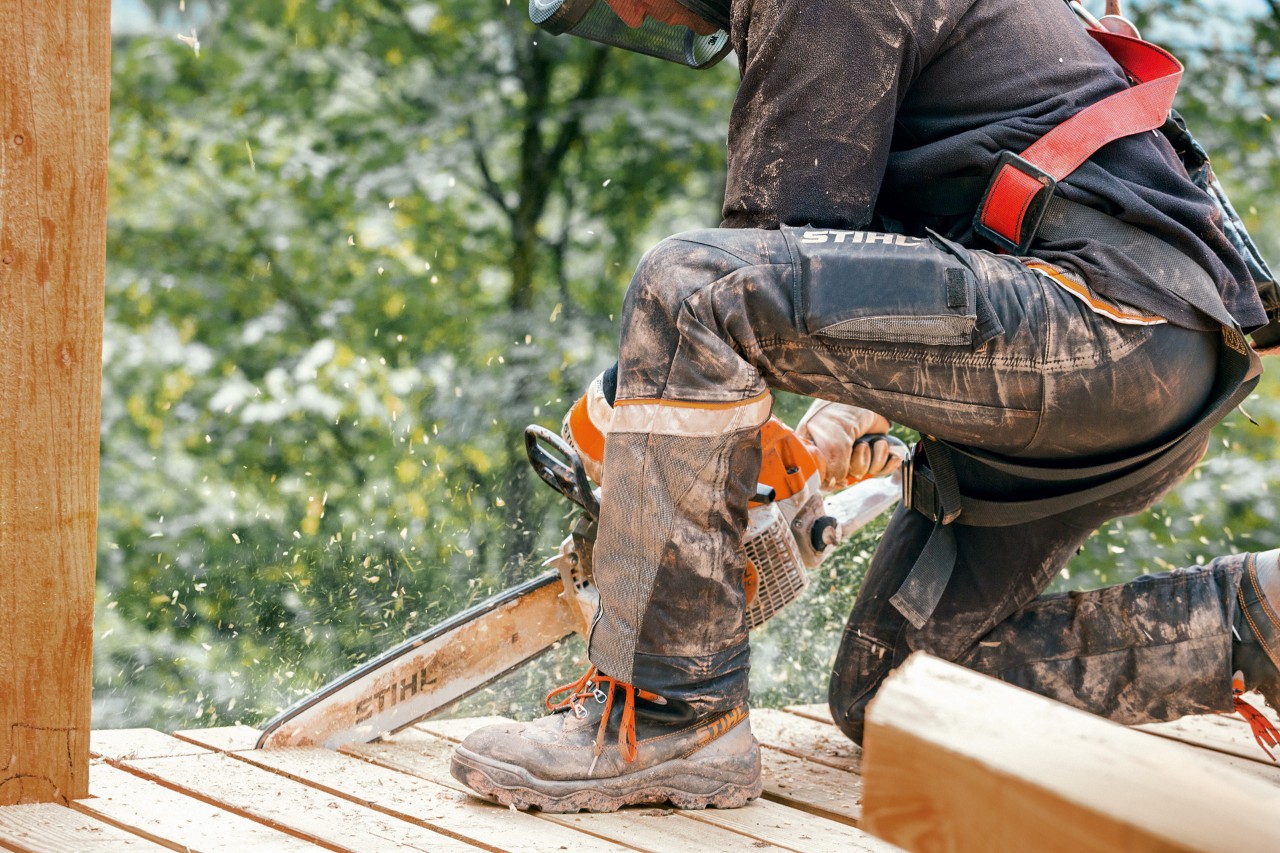 En person iført arbeidsstøvler og STIHL Advance X-Light bukse sager av en kant på en treplatting med en STIHL motorsag
