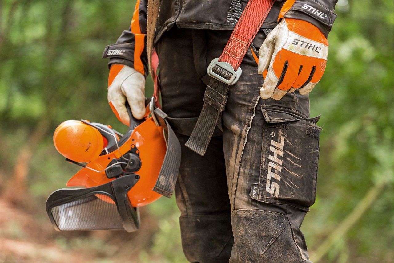 En person med STIHL arbeidsbukser og arbeidshansker som holder en hjelm 