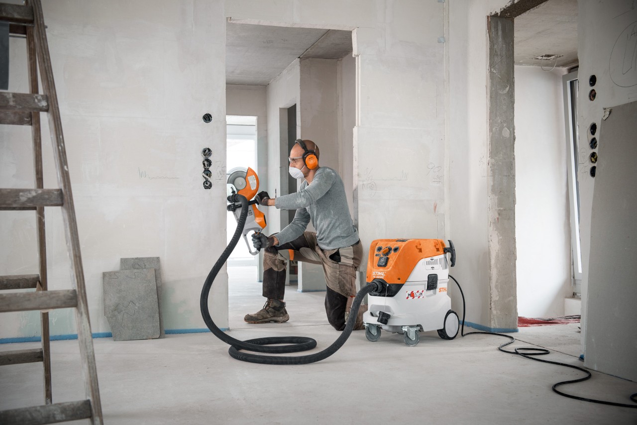 En mann som bruker en STIHL SE 133 ME våt- og tørrstøvsuger mens han arbeider med en STIHL TSA 230 kappemaskin