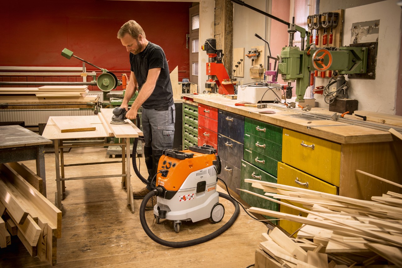 Mann som bruker en STIHL SE 133 ME våt- og tørrstøvsuger i et verksted mens han arbeider med treplanker