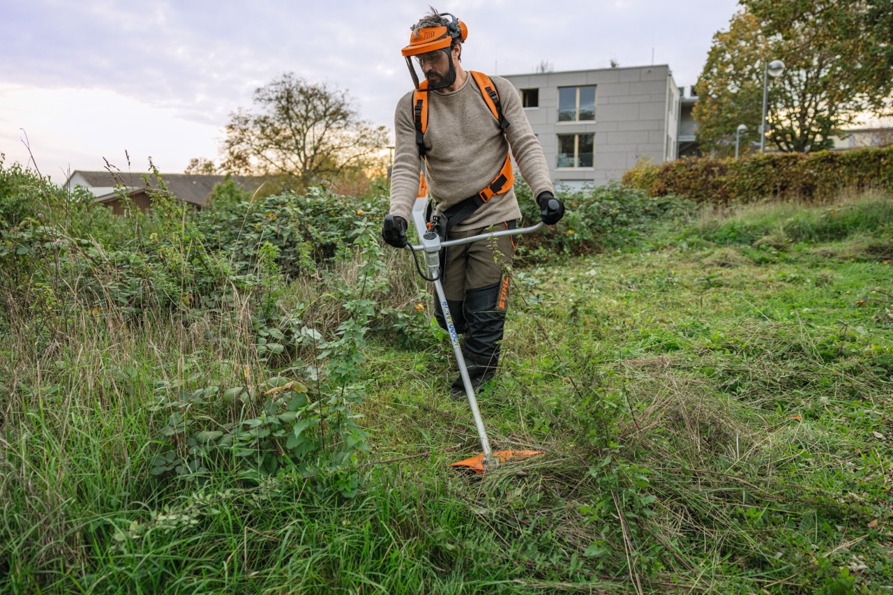 En mann iført STIHL verneutstyr klipper et vil og gjengrodd område med en STIHL FSA 200 batteridrevet ryddesag