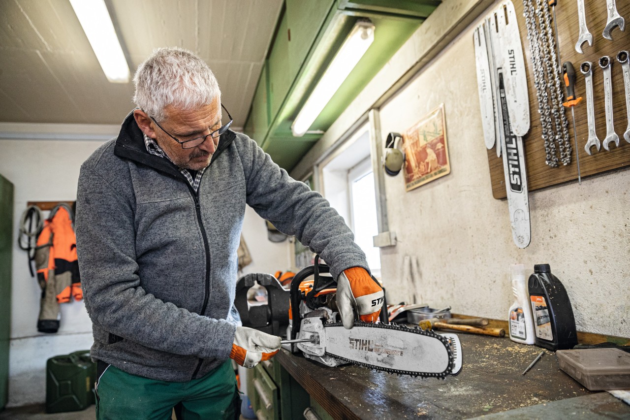 En mann i et verksted fester et STIHL Rollomatic E-sverd fast på en motorsag 