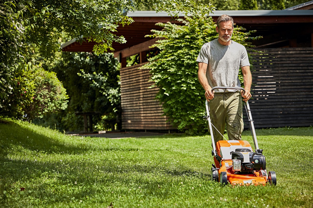  En mann klipper plena riktig med en bensin-gressklipper RM 248 fra STIHL foran et hageskjul