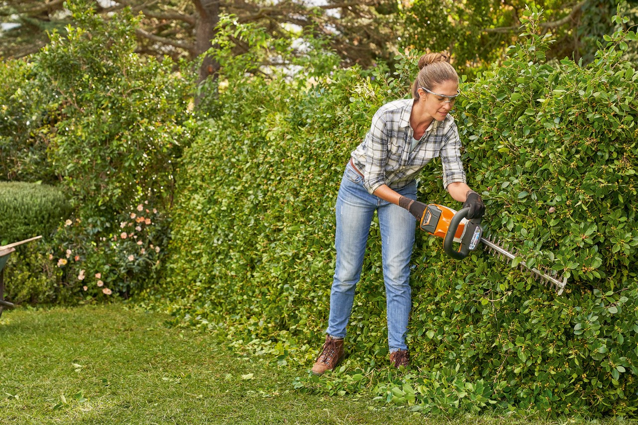 En kvinne bruker hekksaksa HSA 82 fra STIHL til å trimme hekken