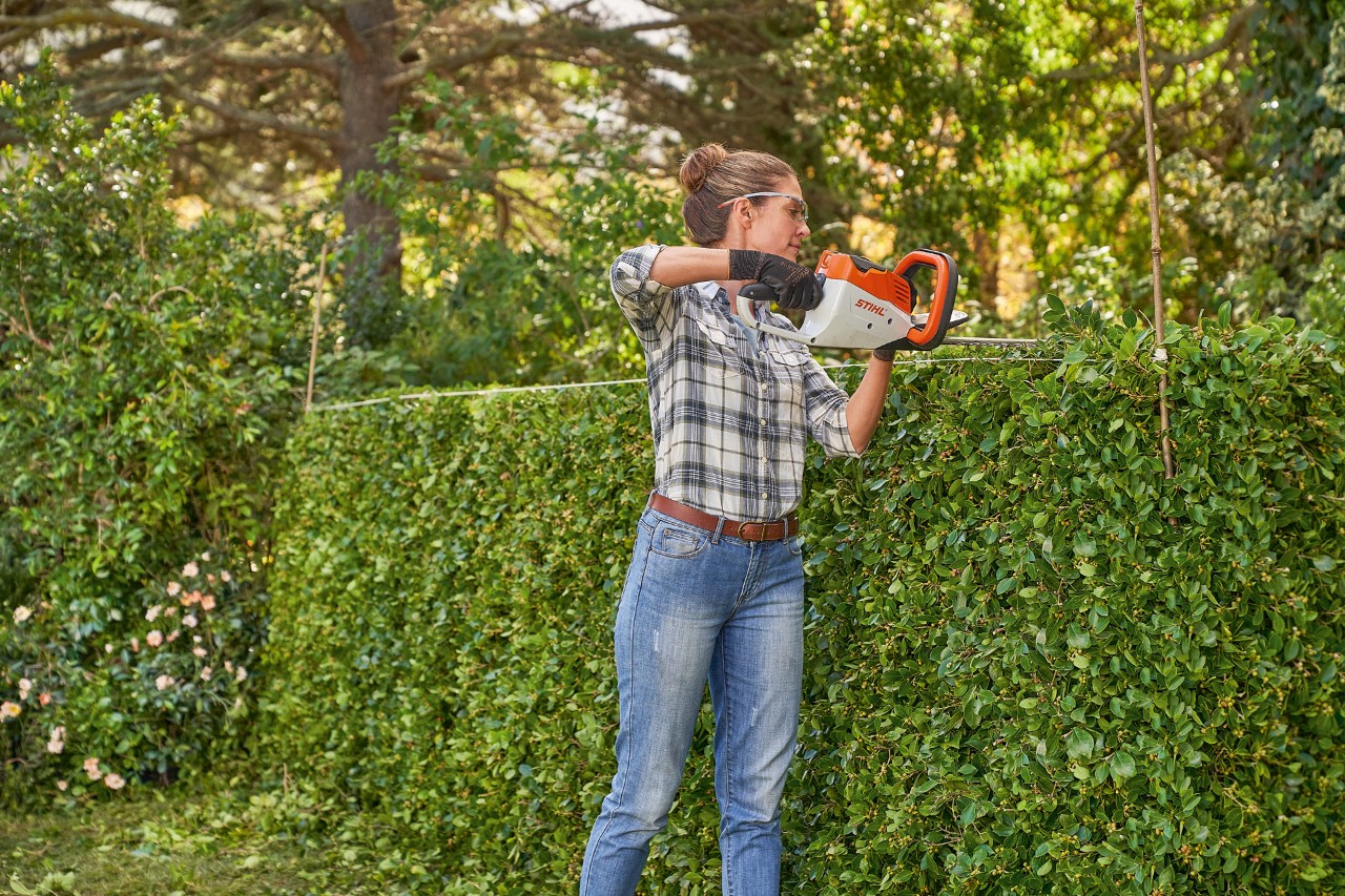 En kvinne trimmer en hekk i form med en batteri-hekksaks HSA 45 fra STIHL