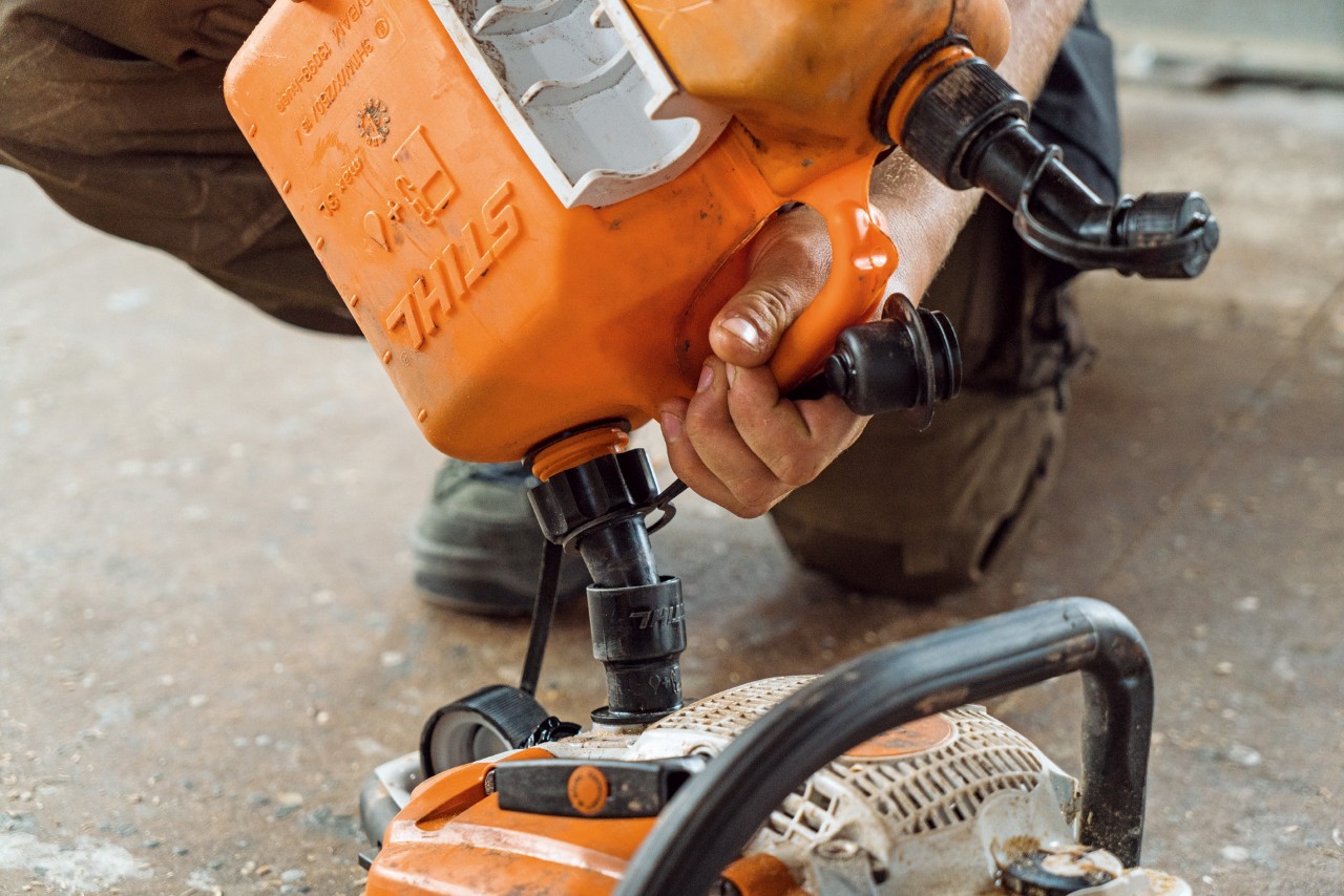 Person fyller bensin på en STIHL motorsag med drivstoffkanne under vedlikehold. 