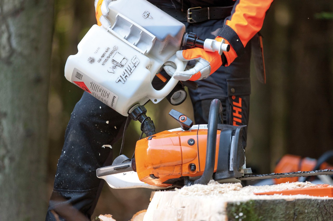 Person fyller drivstoff på en STIHL MS 441 motorsag fra en drivstoffkanne, med vernehansker og beskyttelsesklær. 