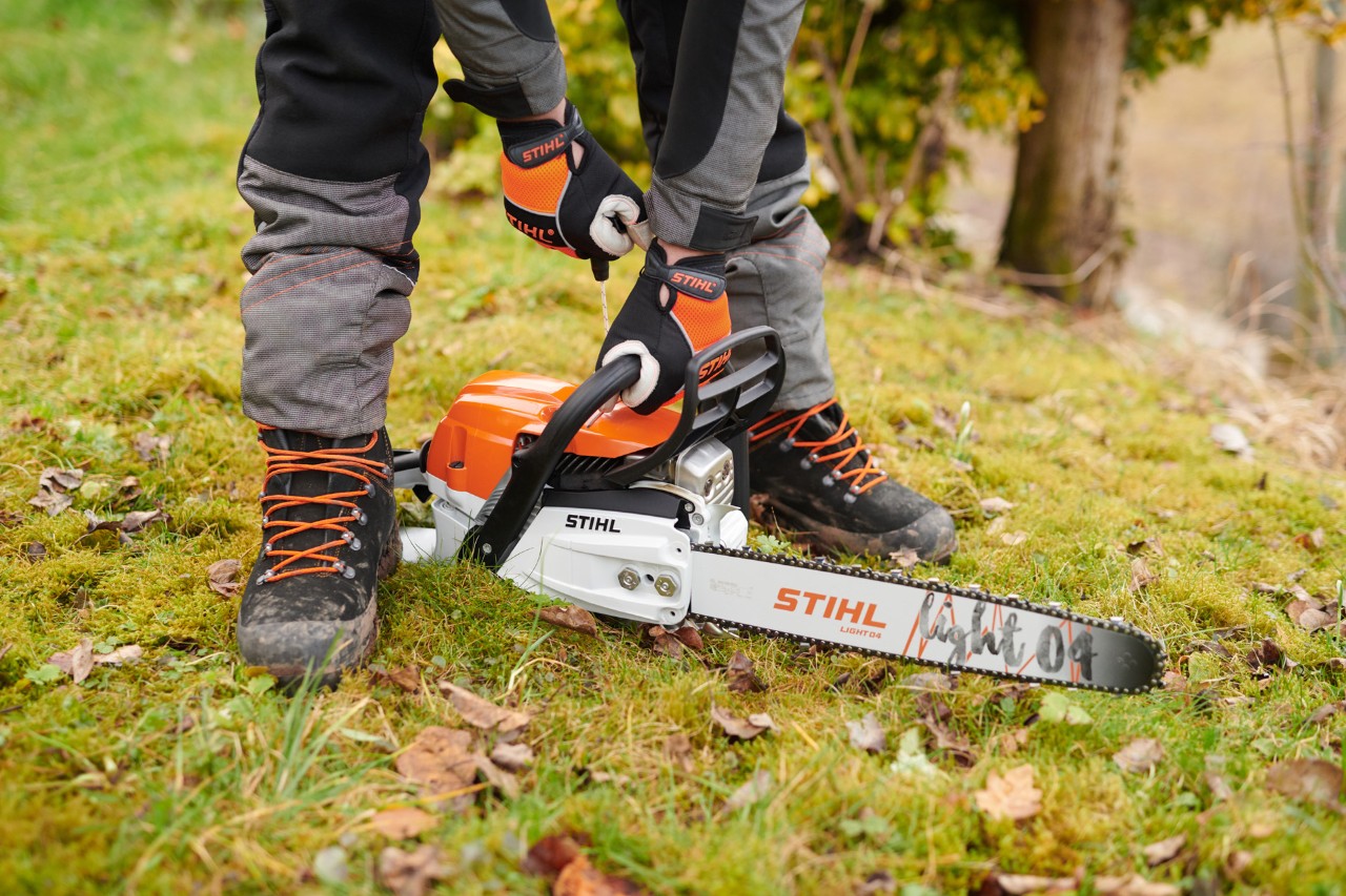 En person med hansker starter en STIHL MS 261 C-M bensindrevet motorsag med et Light 04-sverd