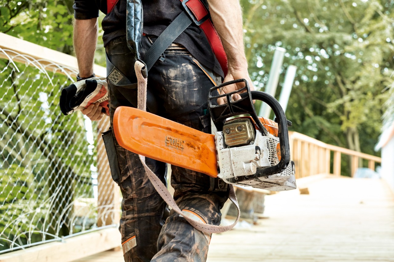 En mann går over en bro med en STIHL MS 261 bensinmotorsag