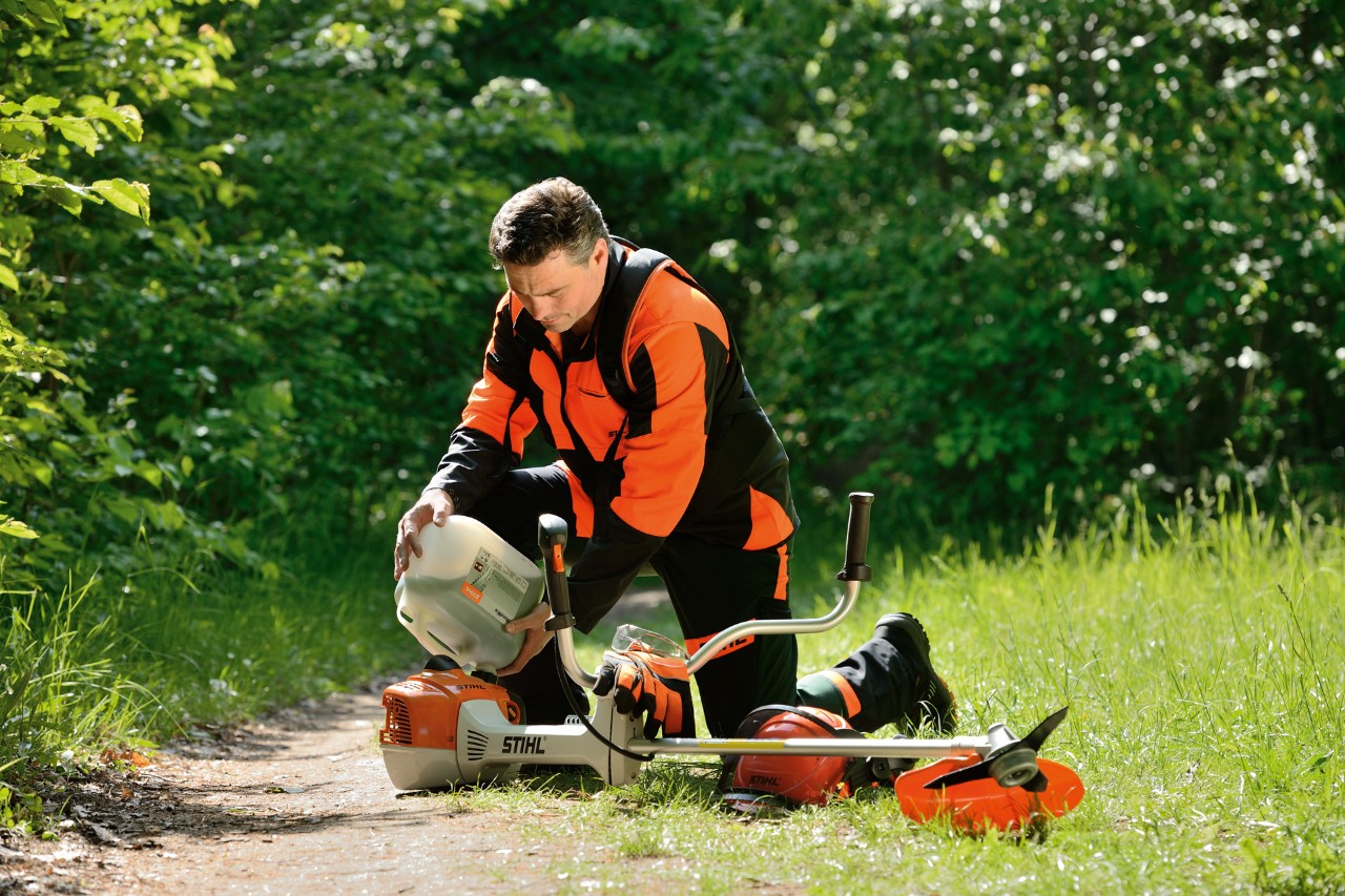 En mann fyller en blanding av bensin og olje på en STIHL ryddesag