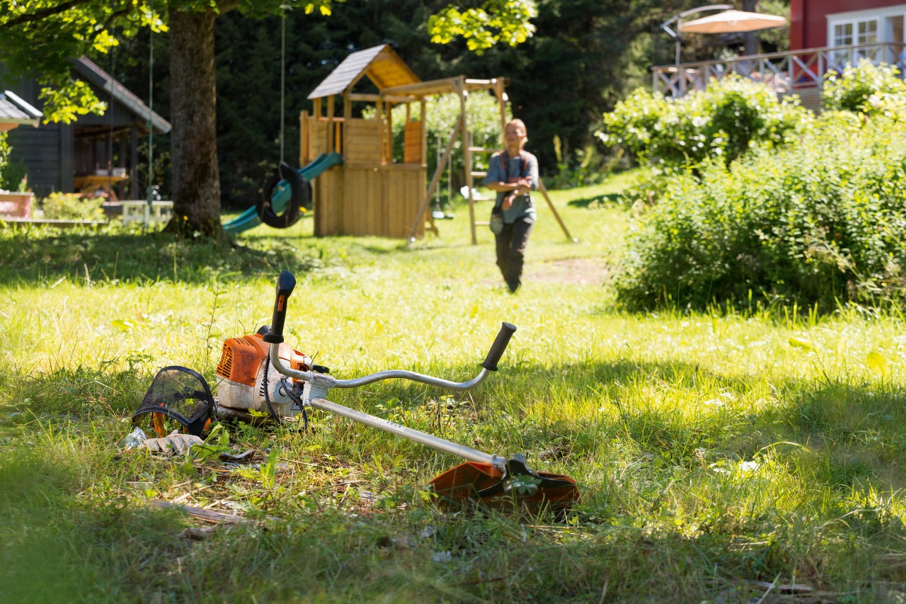 STIHL FS 240 ryddesag i gress og en mann som forbereder vedlikehold i bakgrunnen