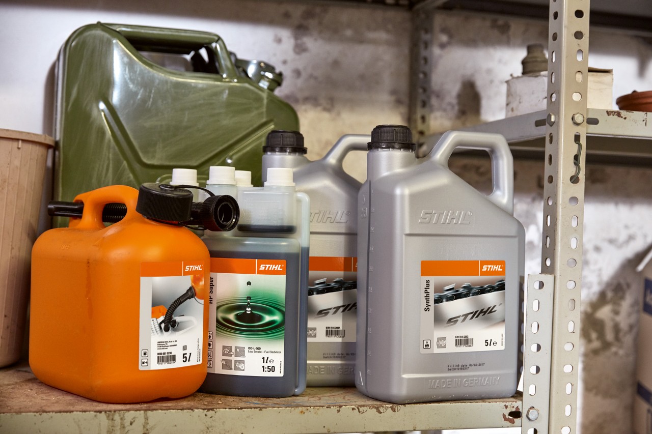 En samling kanner, blant annet en flaske STIHL HP Super 2-takts motorolje og en oransje kombinasjonskanne