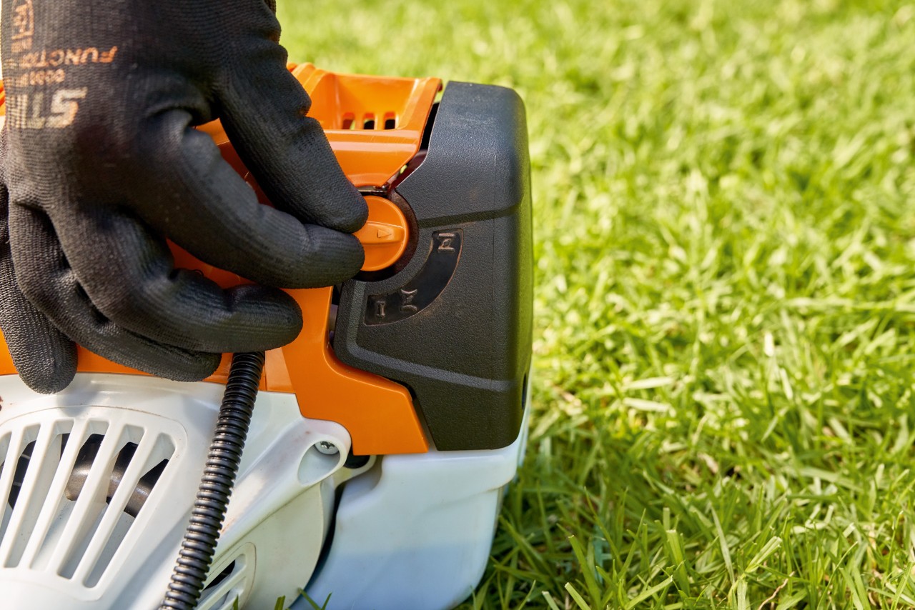 En mann justerer drivstoffpumpe-spaken på en STIHL FS 91 bensindrevet ryddesag for å starte den