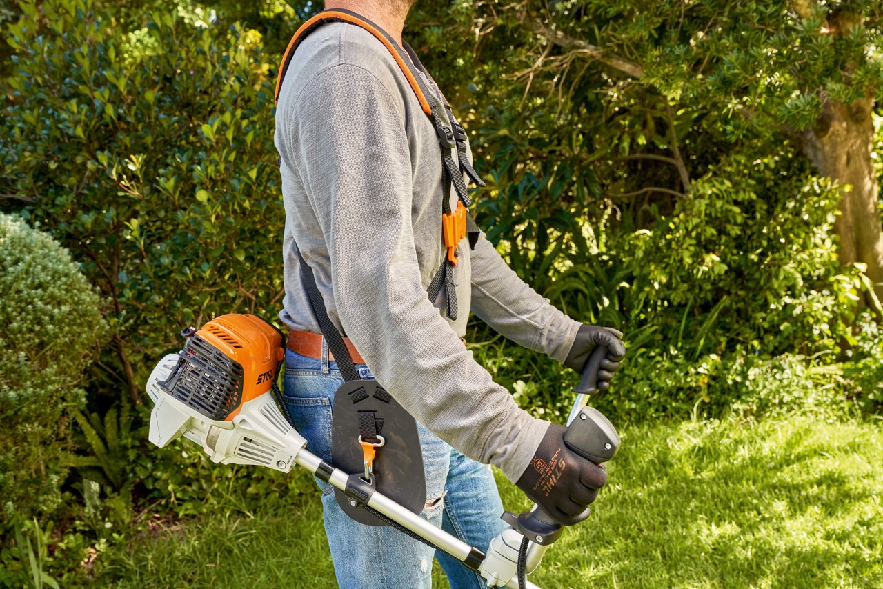 En mann som løfter en STIHL FS 91 bensindrevet ryddesag fra bakken for å begynne å klippe 