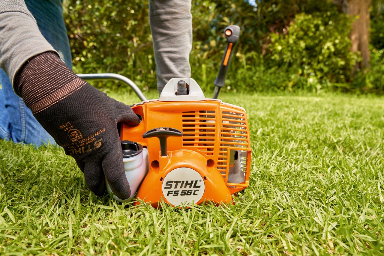 En mann trykker på drivstoffpumpen til en STIHL FS 56 bensindrevet ryddesag for å starte den