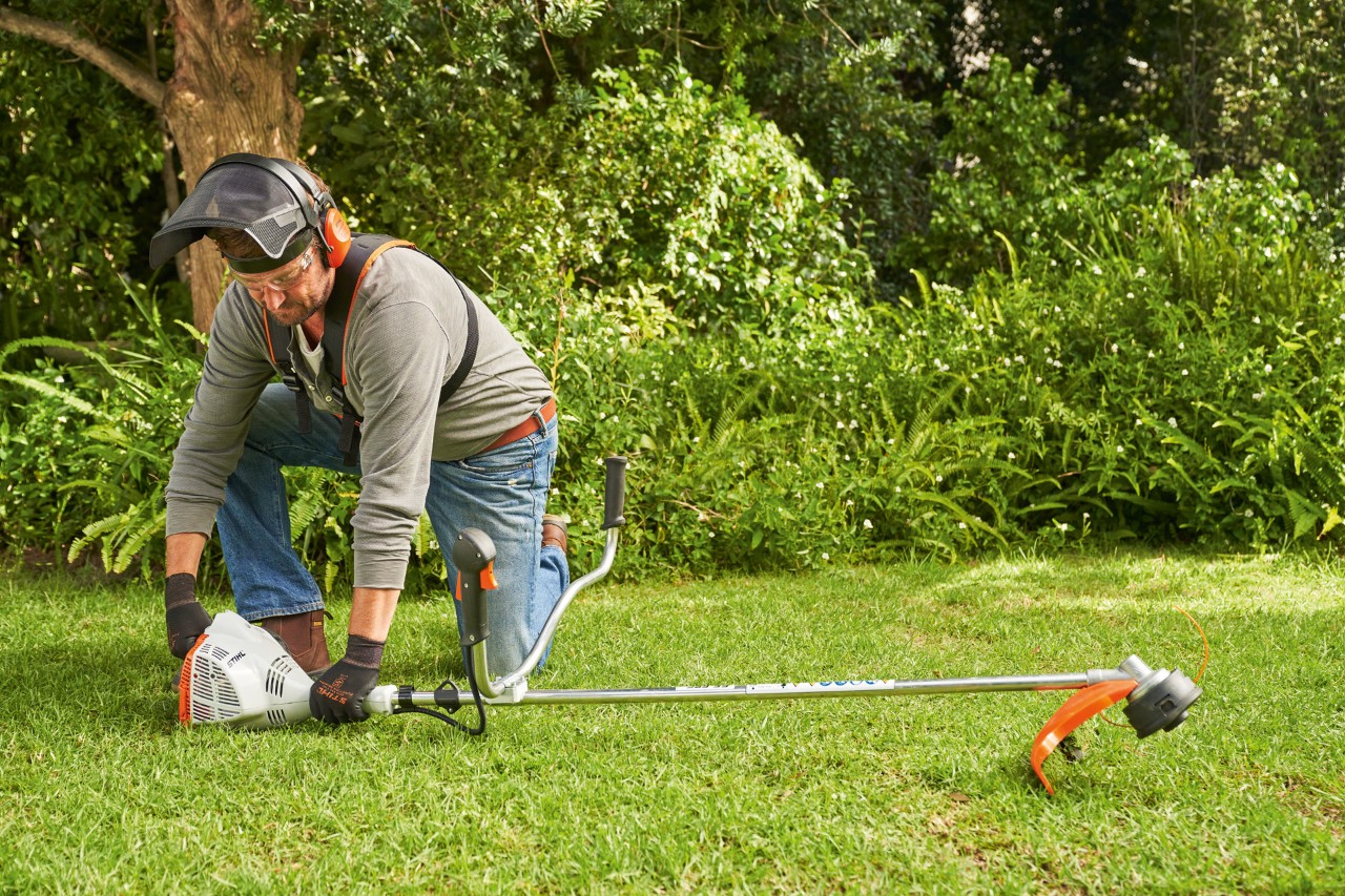 En mann trykker en STIHL FS 56 bensindrevet ryddesag hardt mot bakken før han starter den