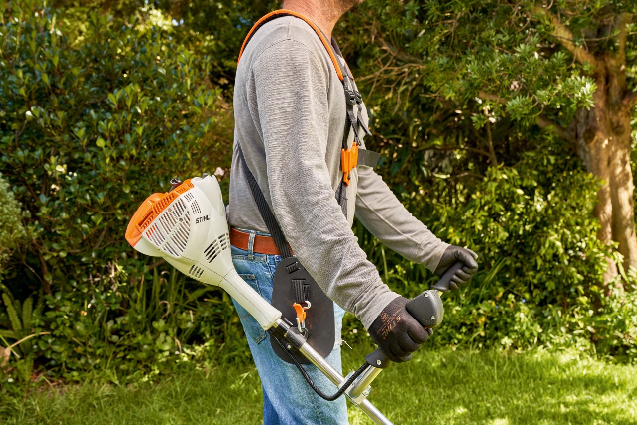 En mann løfter en STIHL FS 56 bensindrevet ryddesag opp fra bakken