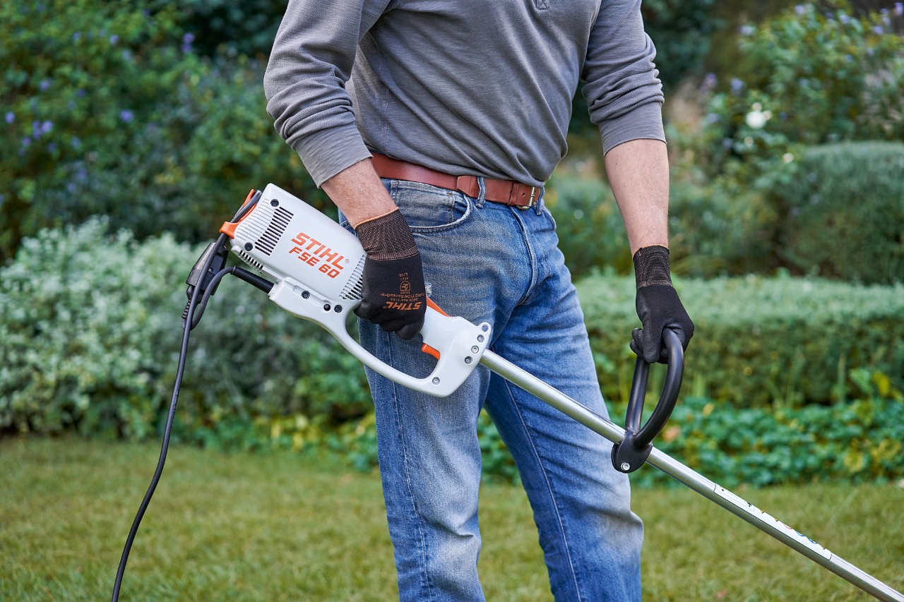 En mann med vernehansker holder en STIHL FSE 60 elektrisk ryddesag med begge hender