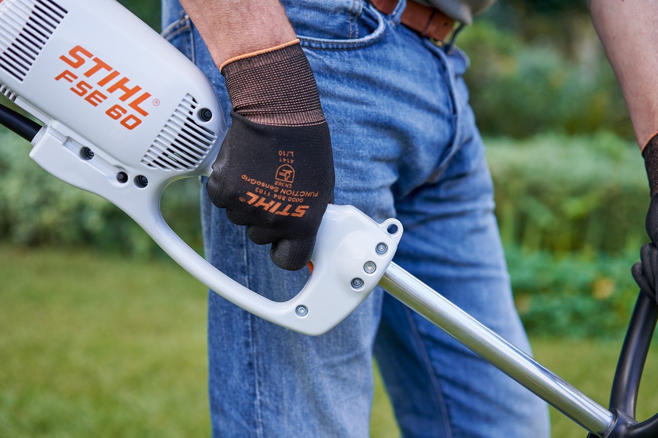 Mann som trykker på bryteren på betjeningshåndtaket til en STIHL FSE 60 elektrisk ryddesag