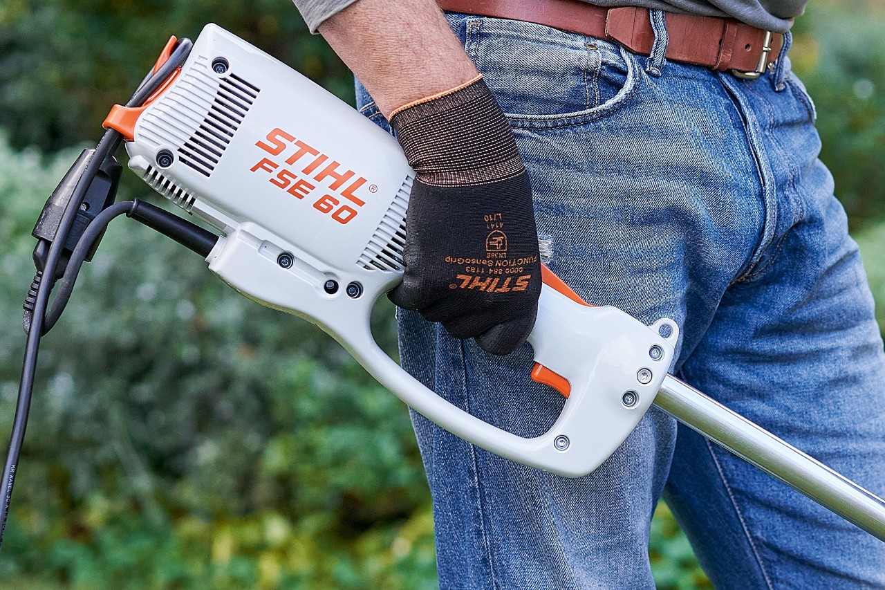 Mann trykker på bryteren for å slå av STIHL FSE 60 elektrisk ryddesag.