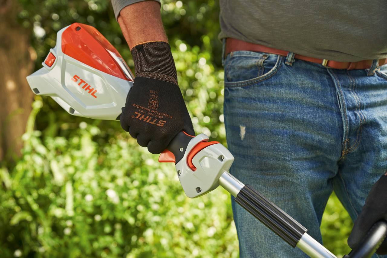 En mann med vernehansker trykker på girspaken på en STIHL FSA 60 batteridrevet ryddesag 