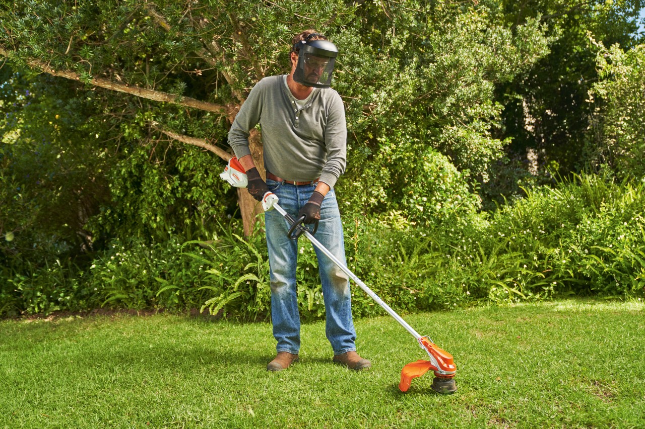 En mann med ansiktsvern klipper gress i en hage med STIHL FSA 60 batteridrevet ryddesag