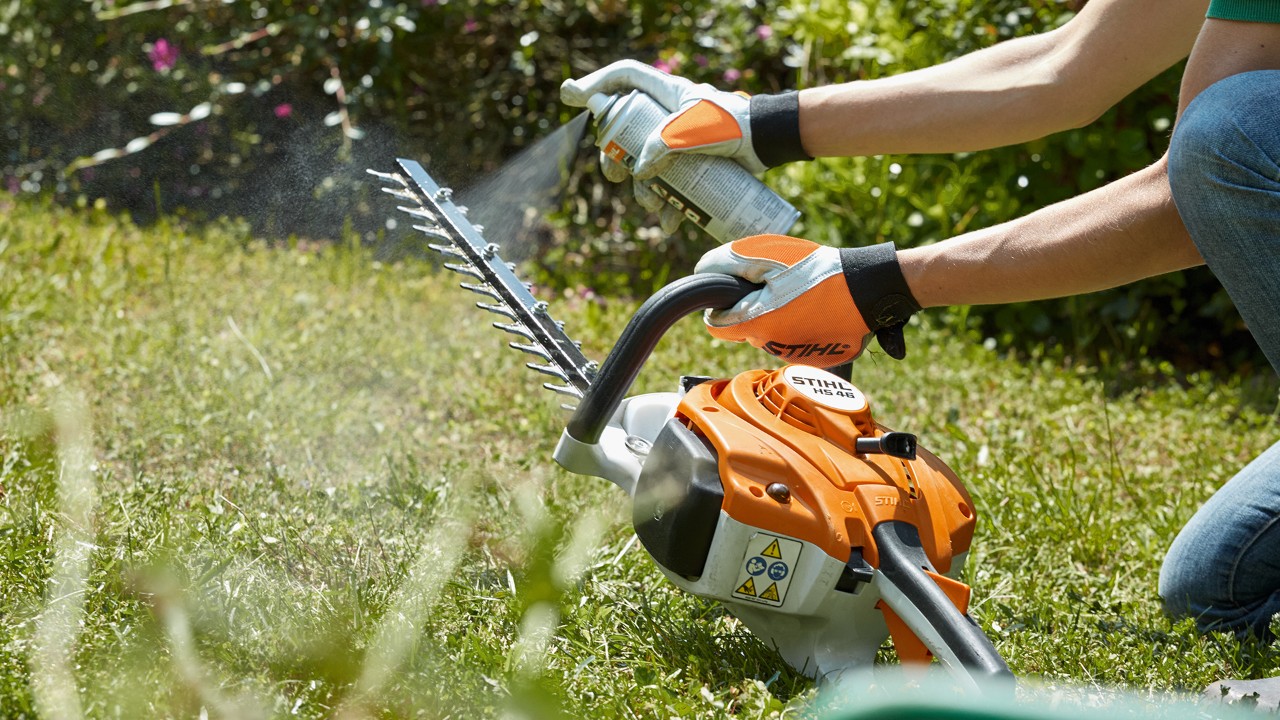 En STIHL HS 82 T bensindrevet hekksaks på en grønn plen sprøytes for rengjøring