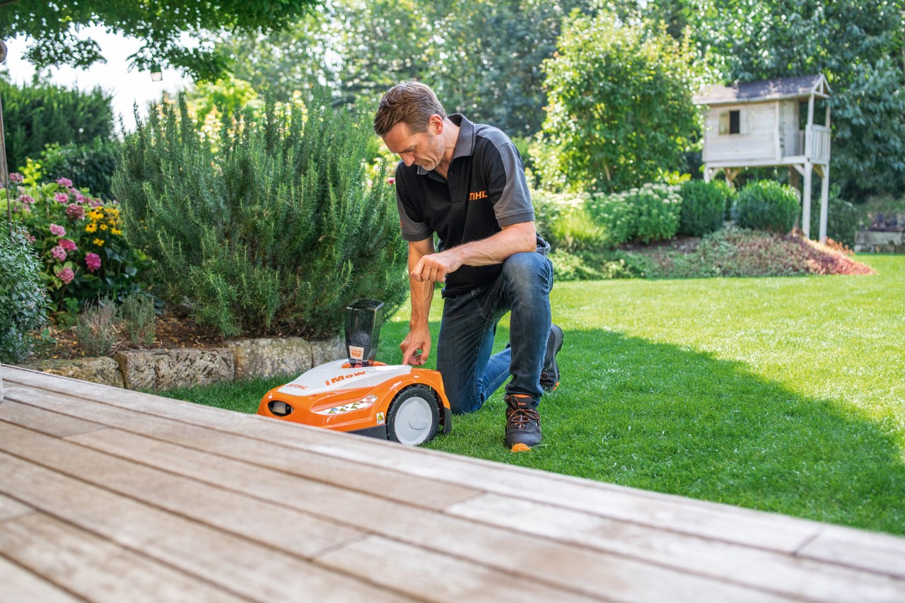 En STIHL-forhandler bruker kontrollpanelet til en STIHL iMOW® 422 robotgressklipper i en hage