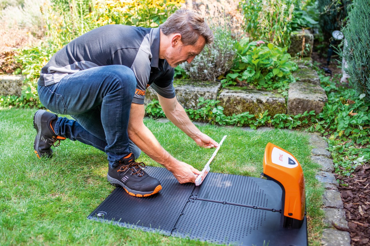 En STIHL-forhandler monterer ladestasjonen til en STIHL iMOW® 422 robotgressklipper i en hage