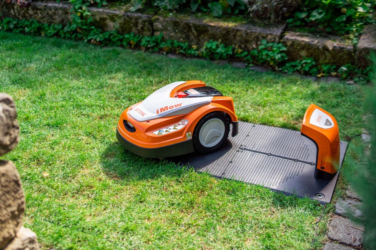 En STIHL iMOW® robotgressklipper ved siden av ladestasjonen på en gressplen