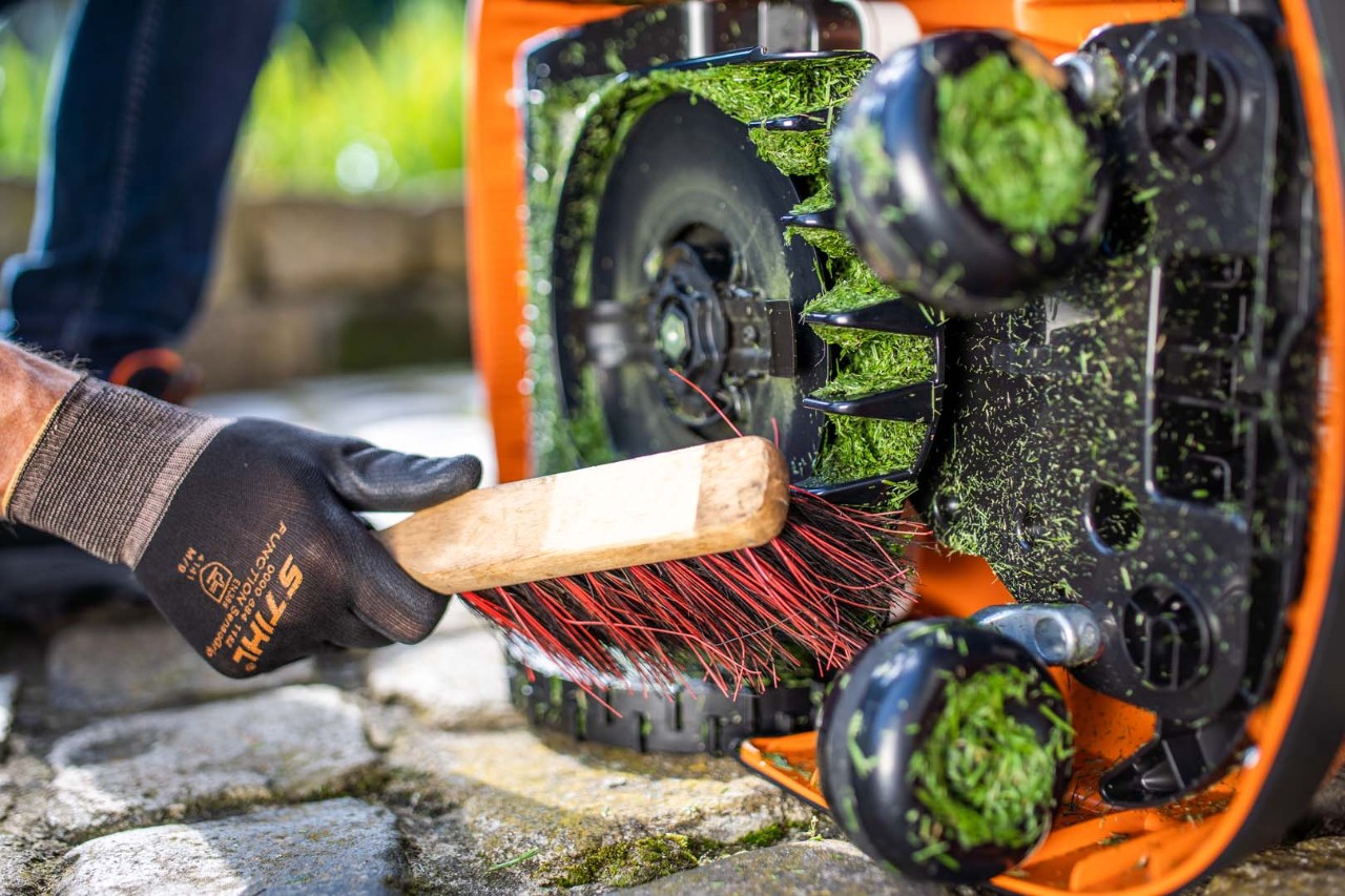 Undersiden av en STIHL iMOW® 422 robotgressklipper rengjøres med kost
