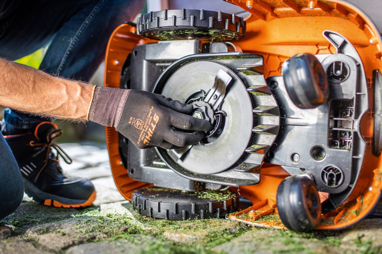En STIHL iMOW® 422 robotgressklipper lagt på siden, mens en person med hansker inspiserer knivbladet