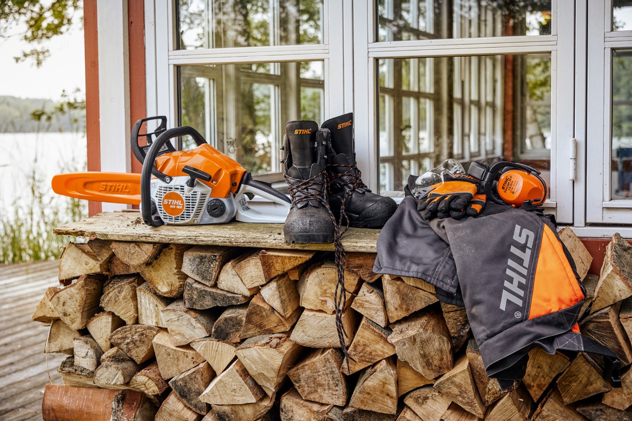 STIHL verneklær og MS 162 liggende på en hylle over en vedstabel