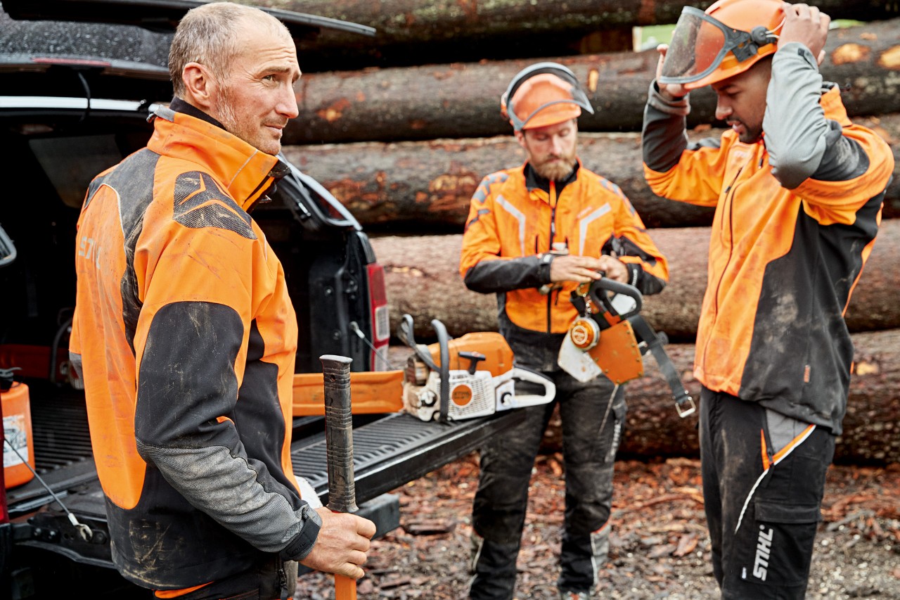 Tre menn i STIHL-verneklær gjør seg klare til å bruke en STIHL motorsag foran en tømmerlunne