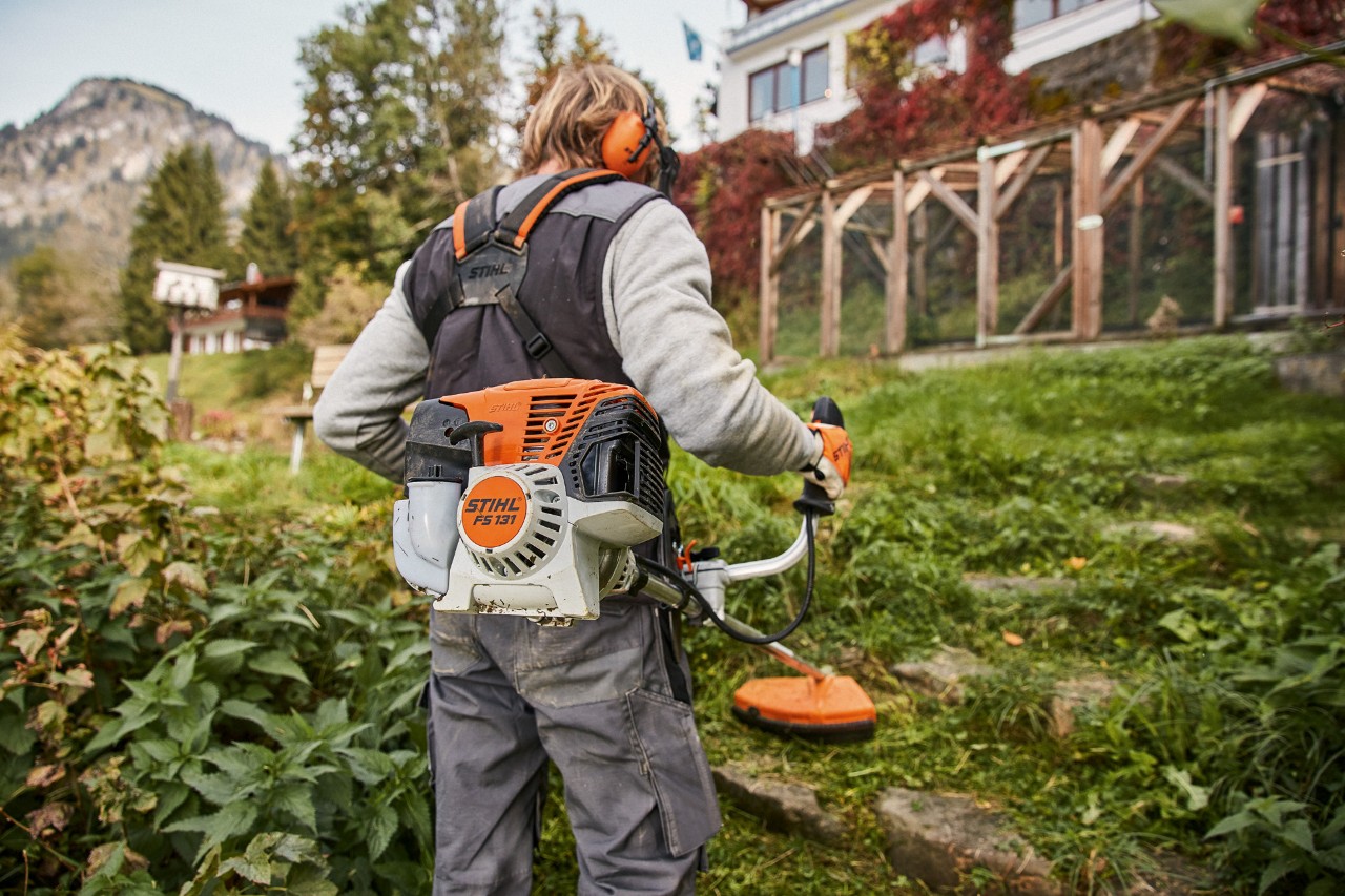 Sluttande mark framför ett hus bearbetas med den bensindrivna trimmern STIHL FS 131 med 4-Mix®-motor
