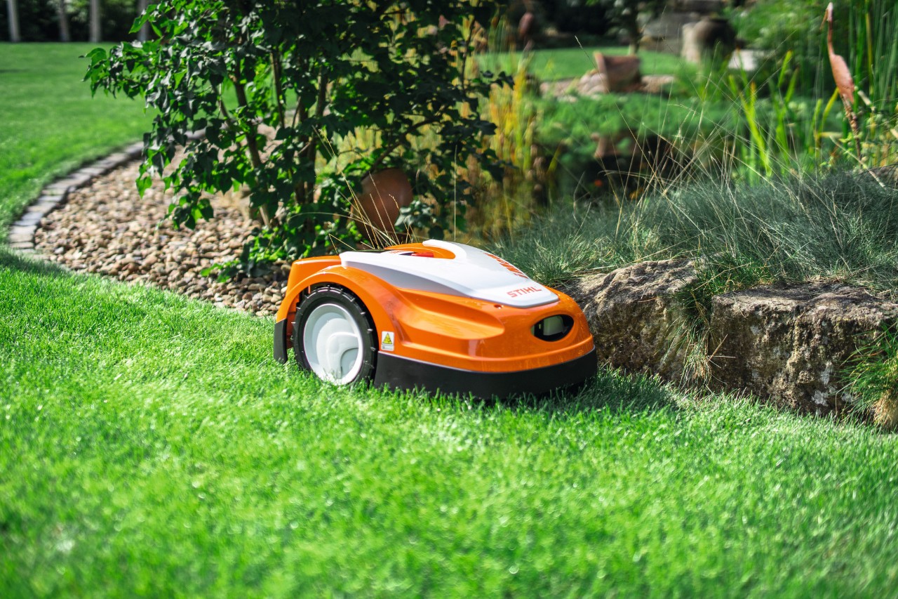 En STIHL iMOW RMI 422 klipper et gressareal i en hage langs en liten steinmur.