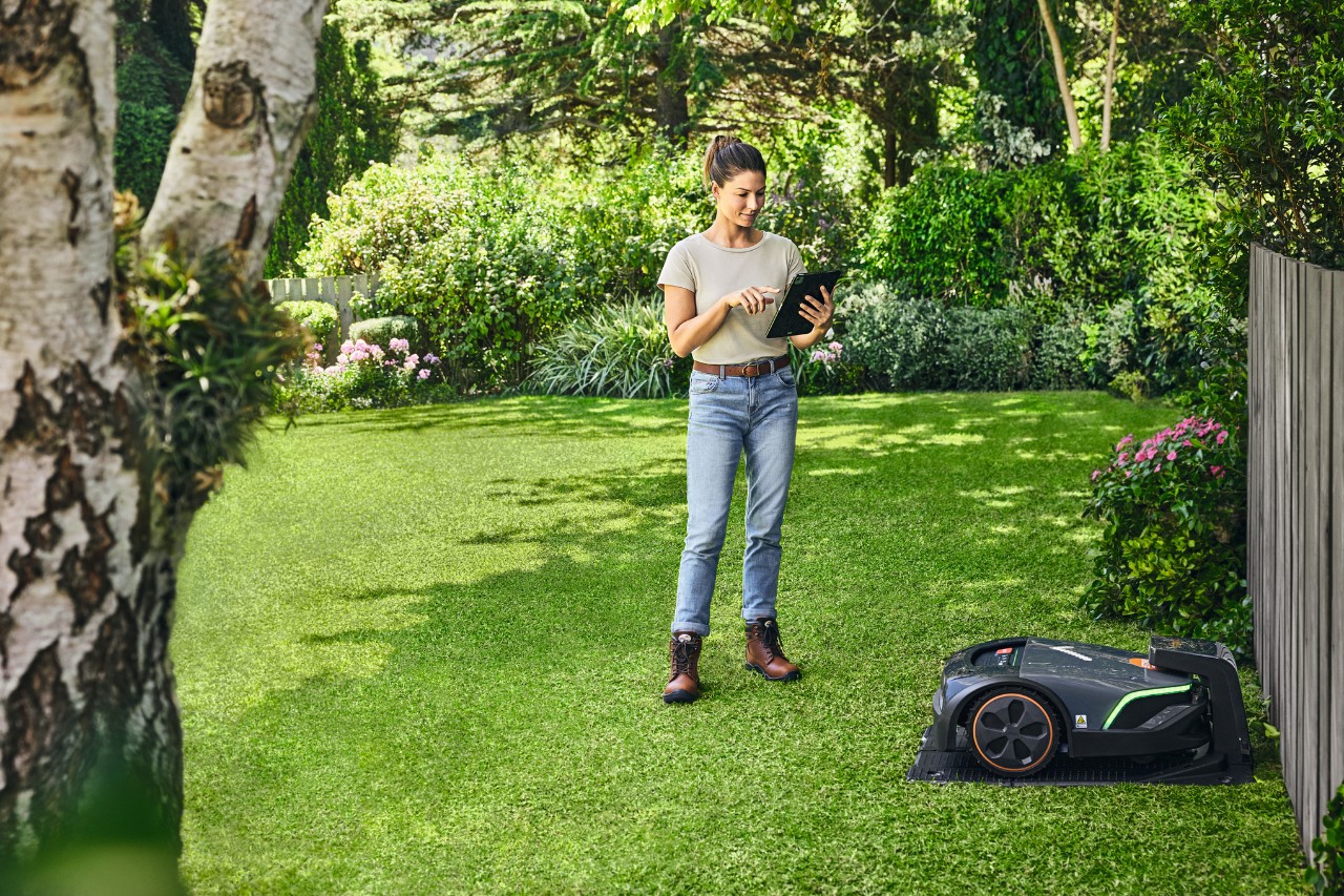 En kvinne som bruker STIHL iMOW® EVO i hagen via et nettbrett