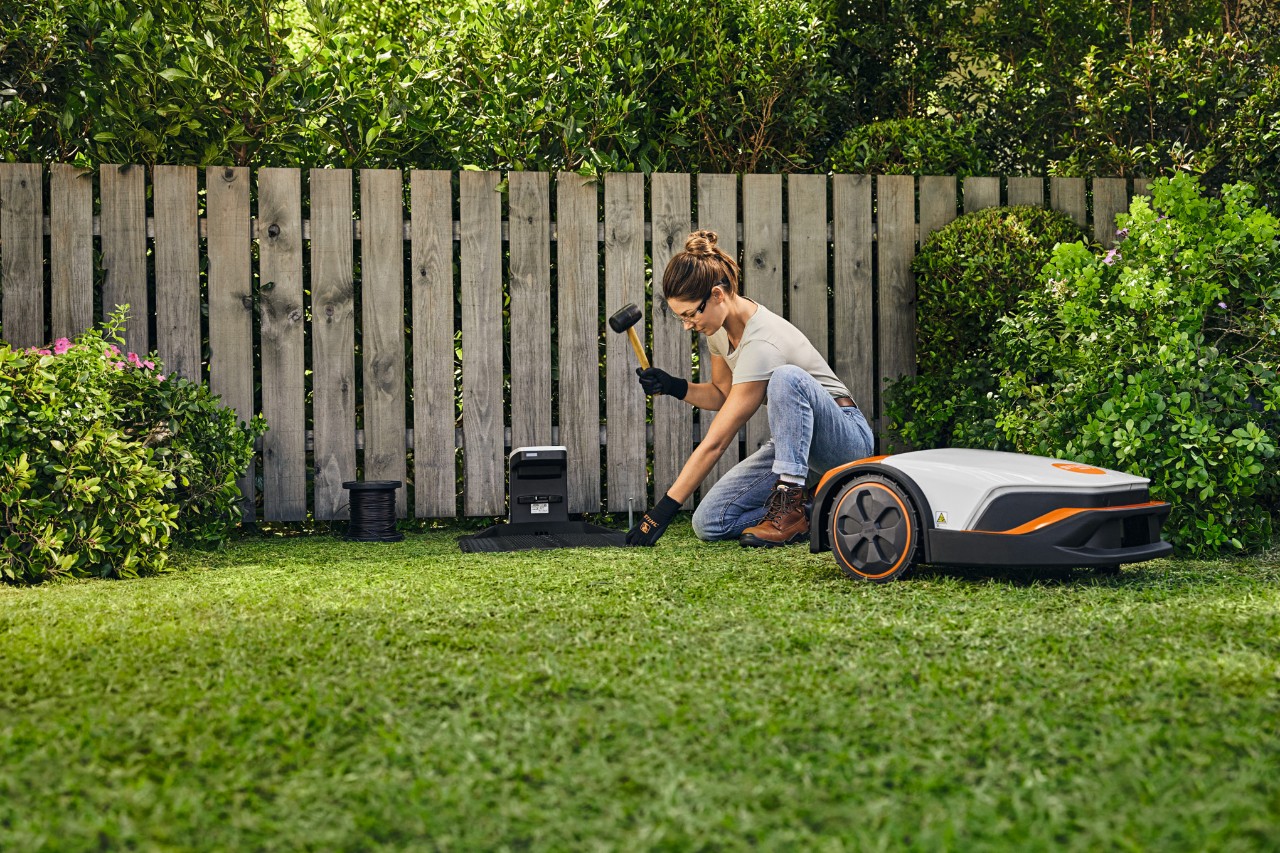 En kvinne monterer dokkingstasjonen til STIHL iMOW® foran et gjerde i hagen sin.
